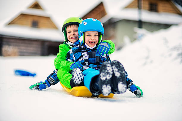 Children having fun riding sled together. Cold winter day. Kids are laughing happily. Boys are aged 6 and are wearing helmets.