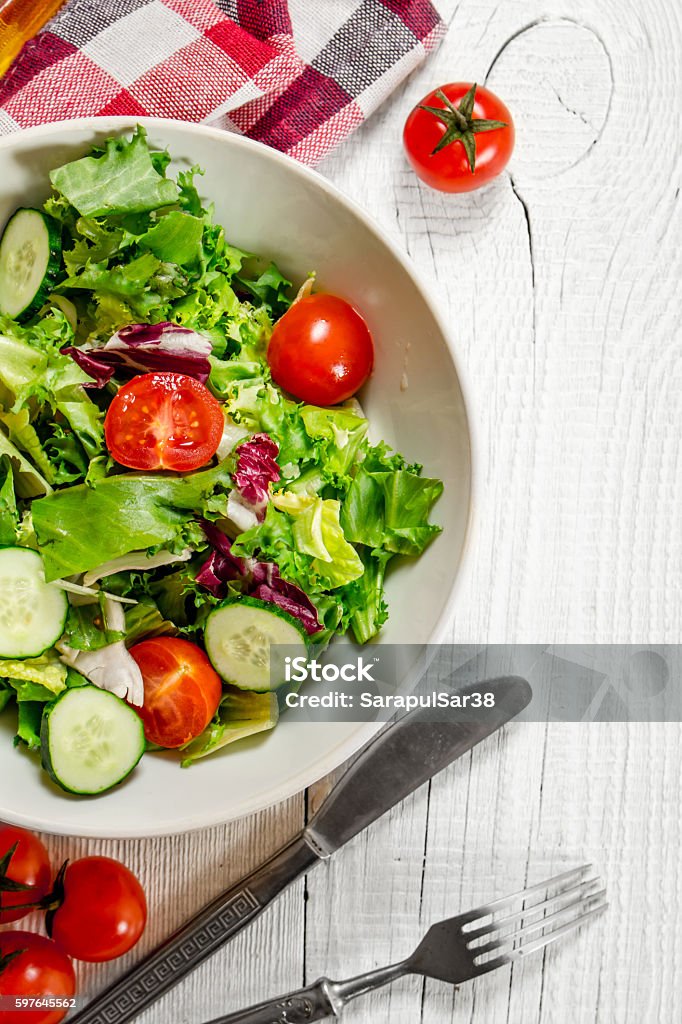 Salad of tomatoes and cucumbers with greens . Salad of tomatoes and cucumbers with greens . On a white wooden background. Arugula Stock Photo