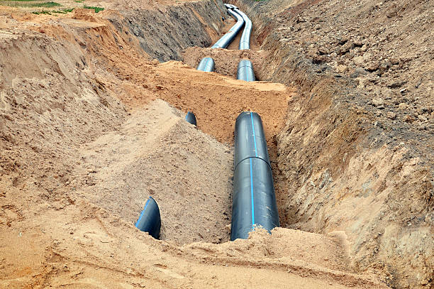 Process of laying of engineering and heating systems. The process of laying of engineering and heating systems. Two black plastic pipes are in a trench of sand in perspective. underground pipeline stock pictures, royalty-free photos & images