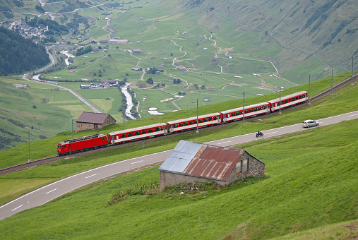 Train of the Matterhorn Gotthard Bahn near Andermatt. The train is on its way from Dissentis in canton Graubünden to Brig in canton Valais and descends from the Oberalp pass in canton Uri. in the background the small village of Hospental
