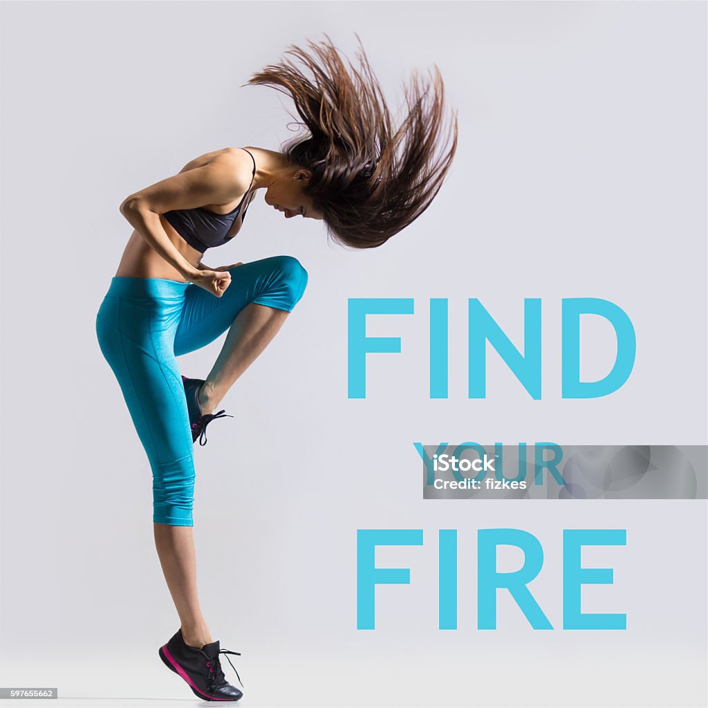 Find your fire Beautiful young fit modern dancer lady in blue sportswear warming up, working out, dancing with her long hair flying, full length, studio image on gray background. Motivational phrase "Find your fire" Exercising Stock Photo
