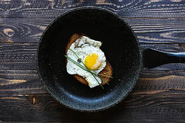 Fried egg in a black pan over a dark old dirty wood background with dramatic light.