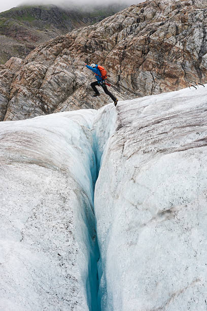 homem pula sobre fenda perigosa com gelo azul - exploration mountain ice jumping - fotografias e filmes do acervo