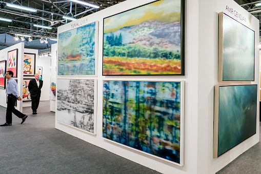 Newyork, USA - April 17, 2016: Appearence from NewYork ArtExpo 2016.  Paintings,pictures,photographs on the wall and two man walking behind the stands and they are looking to the arts. International Artexpo is the worlds largest fine art trade show, providing dealers, collectors and buyers with access to thousands of innovative works from artists and publishers in one single venue.