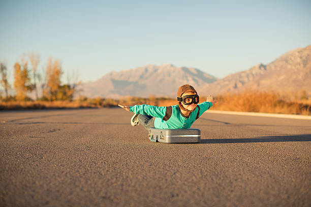 istock Young Boy with Goggles Imagines Flying on Suitcase 597927612