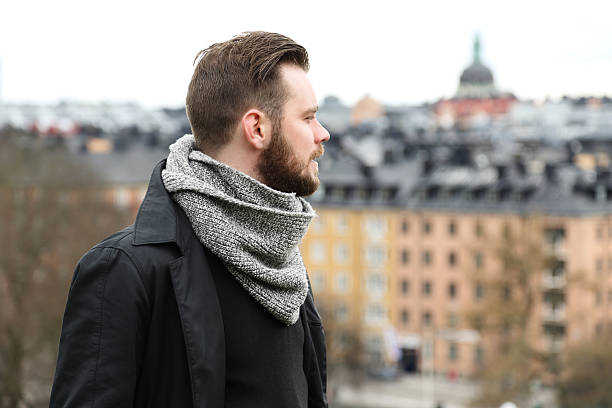 Man looking around with cityscape An attractive man wearing a jacket and a scarf standing high up on a mountain with a cityscape behind him on a cold autumn day. looking around stock pictures, royalty-free photos & images