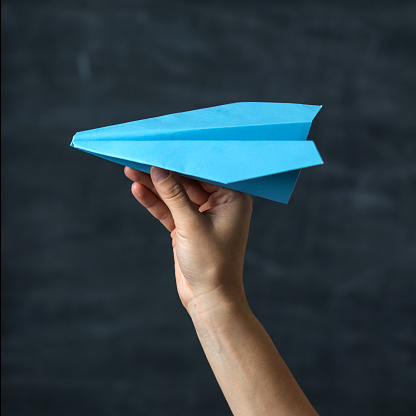 Hand throwing blue paper airplane