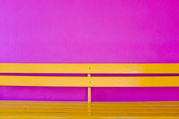 istock yellow wood bench on violet wall background 597940516