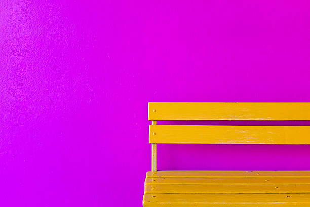 istock yellow wood bench on vivid violet wall background 597940582