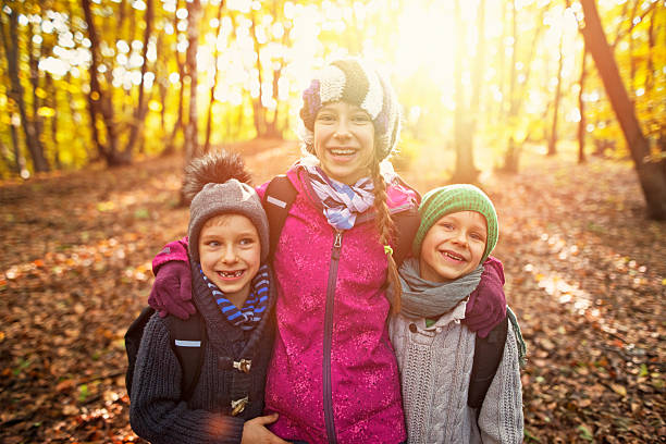 Brothers and sister hiking in autumn forest. The kids are laughing happily. 