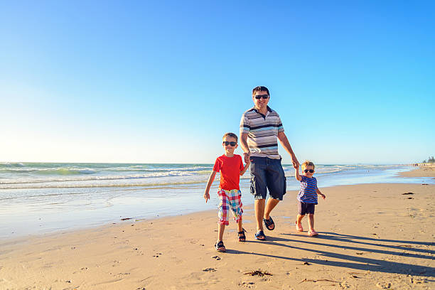 Father and Sons  Walking Together Holding Hands on the Beach at Sunset