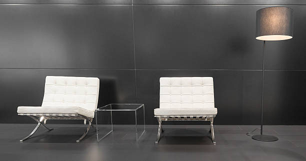 Modern Barcelona design chairs and lamp Brussels, Belgium - January 12, 2016: Pair of white modernist Barcelona design chairs and a modern lamp in front of a grey background. The Barcelona chair was designed by Ludwig Mies van der Rohe and Lilly Reich for the German pavilion for the International Exposition of 1929 in Barcelona. The chairs are on display at the 2016 Brussels motor show. 1929 stock pictures, royalty-free photos & images