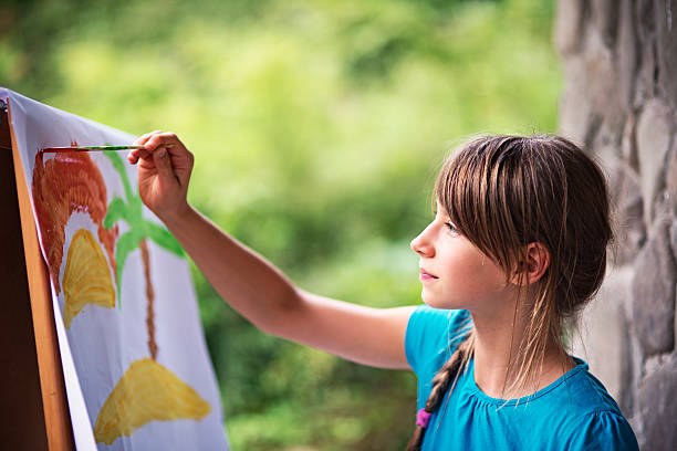 Little girl painting on easel in the garden Little girl having fun painting. She is painting on paper and easel. Girl is aged 10. summer camp photos stock pictures, royalty-free photos & images