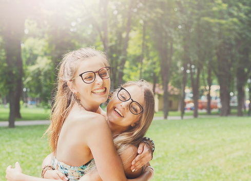 Two happy young girls hug each other. Female friends in eyeglasses embracing, laughing and excited. Woman friendship, walk in the park outdoors