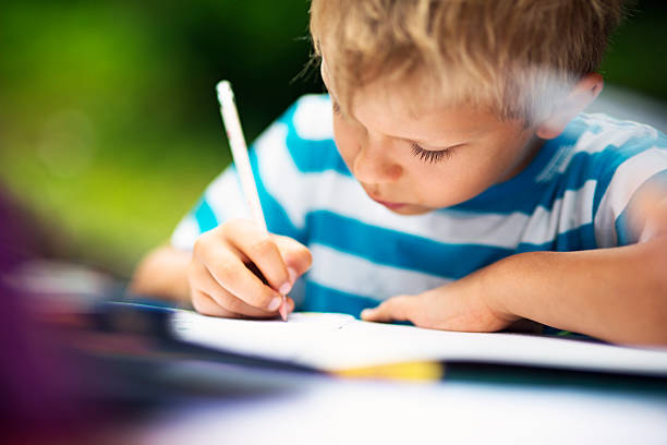 Closeup of little boy doing homework in the garden. The boy is 6 years old and is writing or drawing in the excercise book.
