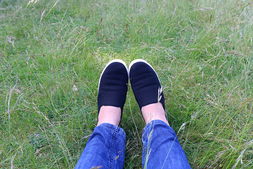 Legs in jeans and black slip-ons in the grass. Selective focus.