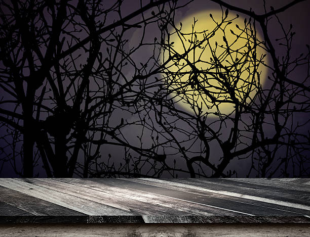 istock Plank wooden table top at spooky tree and full moon 597957580