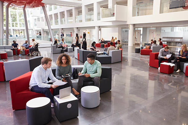 estudiantes sentados en el atrio de la universidad, tres en primer plano - cubicle using computer computer office fotografías e imágenes de stock