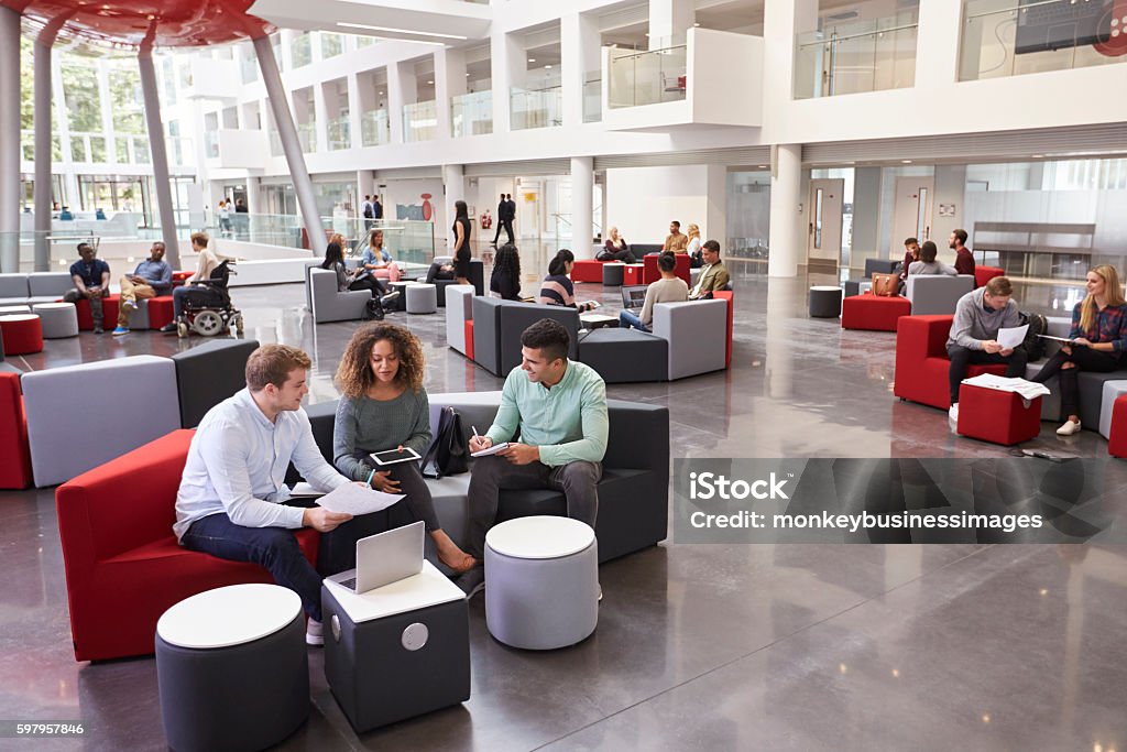 Students sitting in university atrium, three in foreground Modern Stock Photo