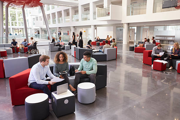 students sitting in university atrium, three in foreground - inside of office technology people imagens e fotografias de stock