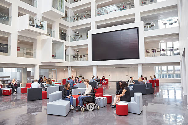 studenten sozialisieren unter av-bildschirm im atrium an der universität - eingangshalle gebäudeteil stock-fotos und bilder