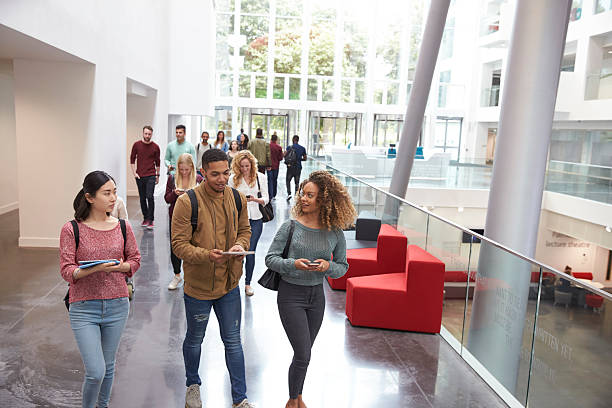 gli studenti camminano e parlano usando i dispositivi mobili all'università - campus school university education foto e immagini stock