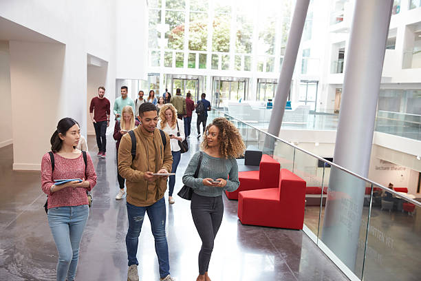 students walk and talk using mobile devices in university - üniversite stok fotoğraflar ve resimler
