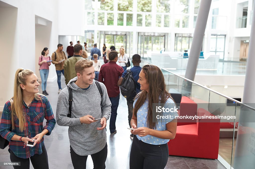 Students holding tablets and phone talk in university lobby University Student Stock Photo