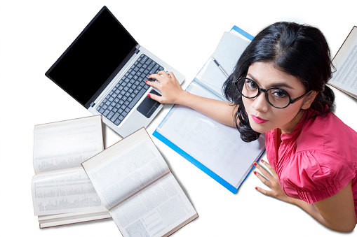 High angle view of pretty student wearing glasses and looking at camera while lying on the floor with laptop and books