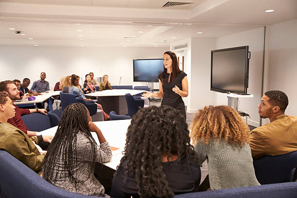 Female teacher addressing university students in a classroom Female teacher addressing university students in a classroom man in the desk back view stock pictures, royalty-free photos & images