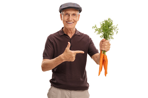 Mature man holding a bunch of carrots and pointing at them isolated on white background