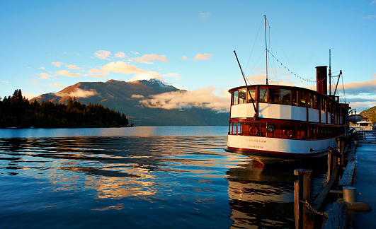 Queenstown, New Zealand - November 10, 2012: Early morning in Queenstown on New Zealand's South Island, and the stately old steamship SS Earnslaw lies moored up at the quayside. Lake Wakatipu stretches away into the distance where it meets the hills & mountains of the Southern Alps.