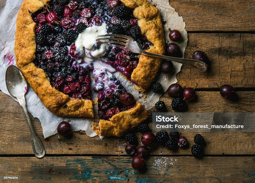 Garden berry crostata sweet pie with melted vanilla ice-cream Homemade garden berry galetta or crostata sweet pie with melted vanilla ice-cream scoop on rustic wooden background. Top view, horizontal composition Crostata Stock Photo