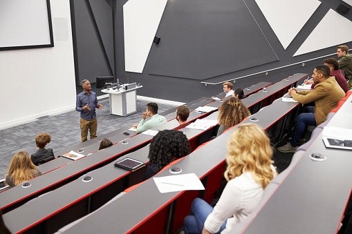 Standing in front of the large projection screen, the young adult female speaker listens to a question during the seminar.