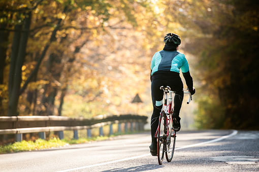 Young handsome sportsman riding his bicycle outside in sunny autumn nature, rear view