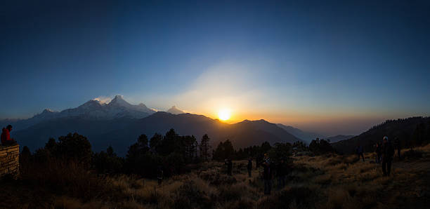 Sunrise shot from Poon Hill in the Nepal Himalayas. The mountains visible in thie image are (L to R) Nilgiri South, Baraha Sikhar, Annapurna South, Hiunchuli & Machhapuchhre. The sky is blue and clear and other people are in the photo watching the sun rise.