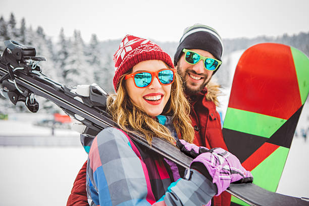 Always for active holidays Couple on vinter vacation at mountain. Holding skis and preparing for skiing. Mountain is coverd with snow. snowboard stock pictures, royalty-free photos & images
