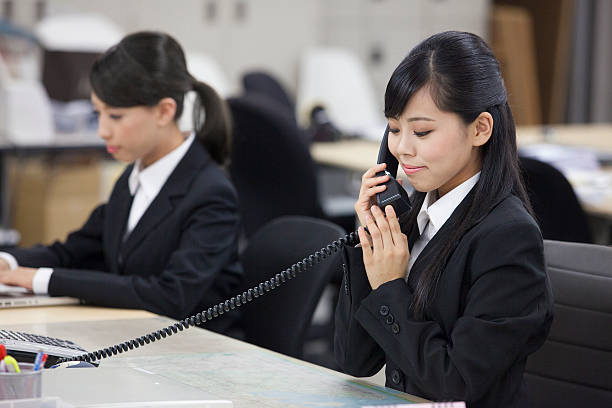 An Asian woman is using giving a good thumbs up while landline phone in the office