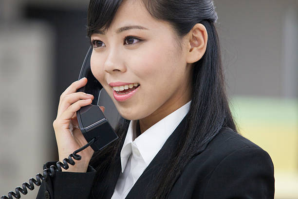 Beautiful young Asian woman in work clothes working on a laptop while talking on the phone in the office