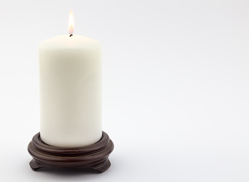 Single white lit candle on wood stand isolated on white background