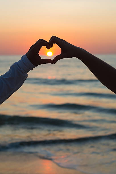 istock Couple doing heart shape with their hands on beachside 597972030