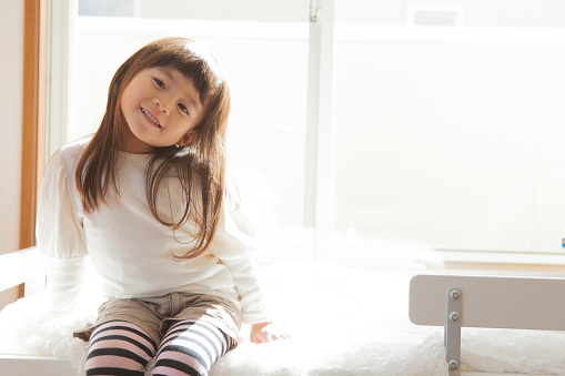 Young Japanese girl sitting in sunlight on a bed