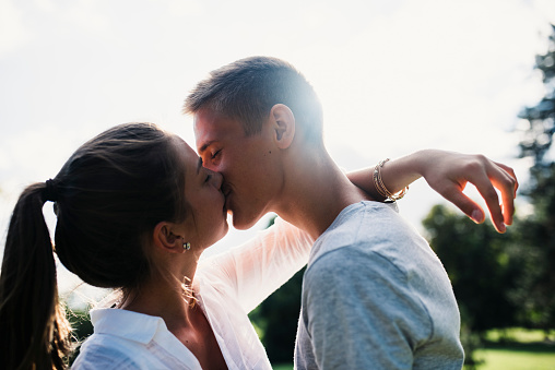 Young couple kissing outdoors in a park. Sun is shining from back.