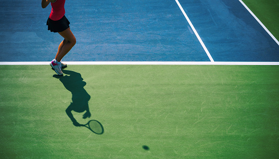 Woman in black outfit training under a harsh sun on a clay court.