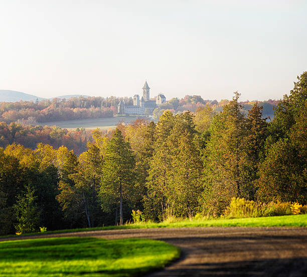 Quebec Estrie Autumn landscape with abbey Quebec Estrie Autumn landscape with abbey Saint-Benoît du lac in the distance. A blured winding road is in the foreground. sherbrooke quebec stock pictures, royalty-free photos & images