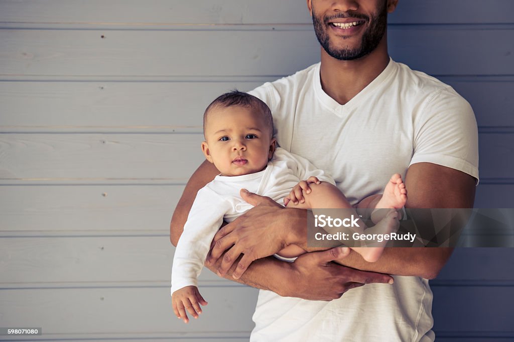 Father and baby Cropped image of handsome young Afro American father smiling while holding his sweet little baby in arms 12-17 Months Stock Photo