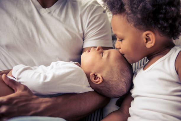 Afro American family Beautiful young Afro American family spending time together. Little baby is sleeping in dad's arms while her sister is kissing her sibling stock pictures, royalty-free photos & images