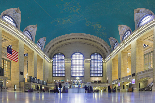 New York, USA - February 21, 2016:  The main concourse of the Grand Central Station is a monumental space and usually filled with crowds. The American flag was hung a few days after the September 11 attacks. The main information booth is in the center of the concourse with a  clock on top designed by Henry Bedford (c. 1913).
