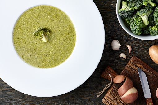 White plate with broccoli soup and ingredients on dark wooden background