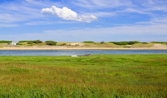Landscape with Meadow, Beach, Rowboat and River, Ogunquitt, Maine, New England, USA. Green grass, trees, water and vivid blue sky with clouds are in the image.